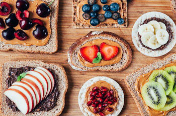 Brotscheiben, die mit einem Brotaufstrich bestrichen sind und mit Bananen, Heidelbeeren, Erdbeeren oder anderem Obst kreativ belegt sind.