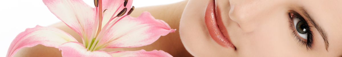 Das Gesicht einer entspannt lächelnden jungen Dame neben einer rosafarbenen Lilienblüte